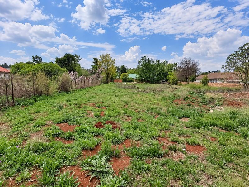 A vacant residential plot featuring natural grass cover, mature trees, and perimeter wire fencing, offering a clear space for potential development.