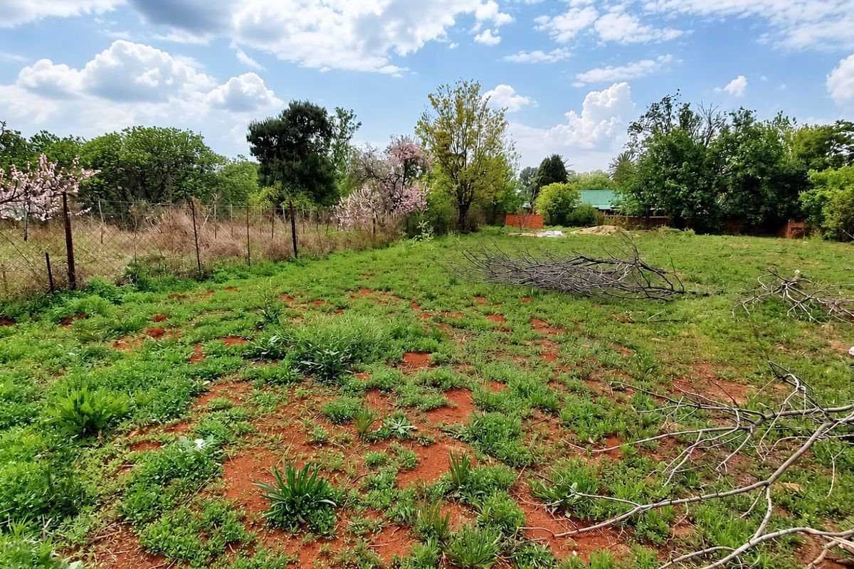 A view of a vacant residential plot featuring natural vegetation, mature trees, and perimeter wire fencing.