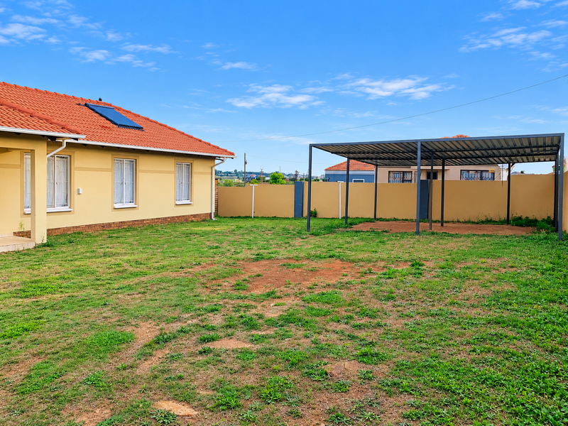 Spacious rear garden featuring a large carport, perimeter walling, and a house equipped with a solar water heating system.