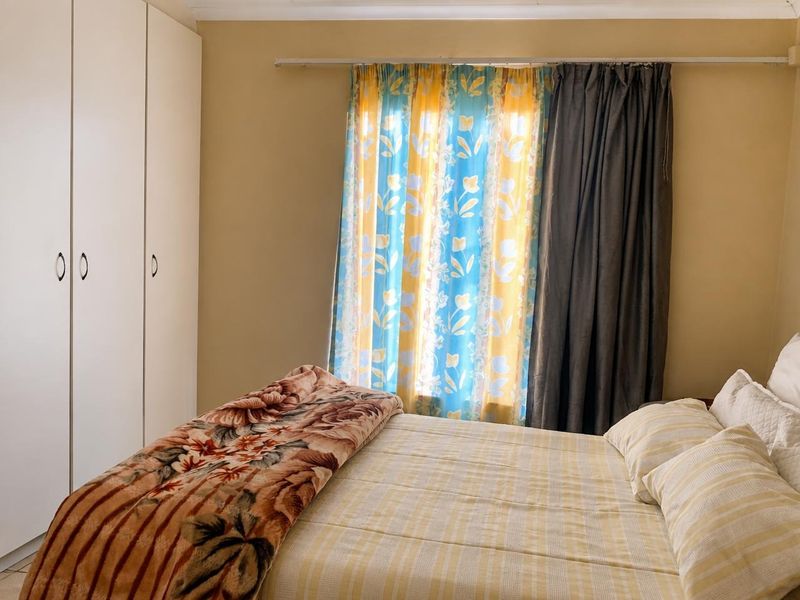 A functional bedroom featuring built-in cupboards and a window with curtain rod, offering a neutral base for potential interior updates.