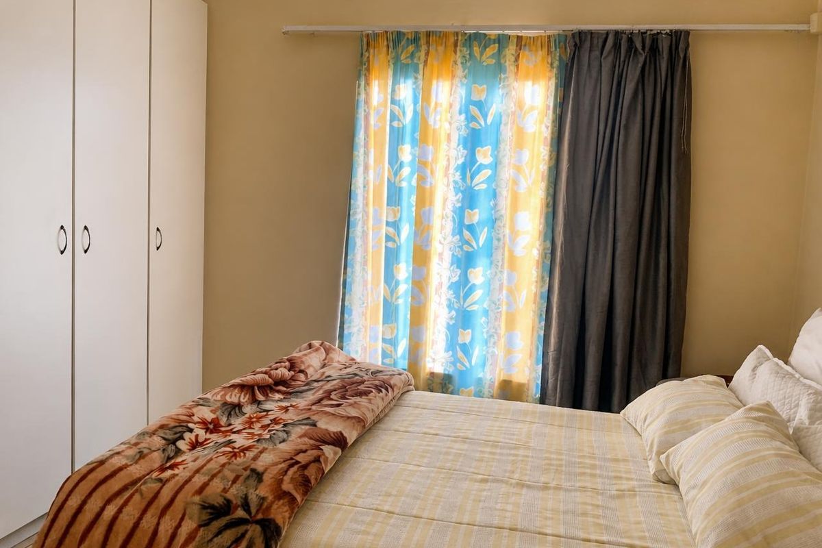 A functional bedroom featuring built-in cupboards and a window with curtain rod, offering a neutral base for potential interior updates.