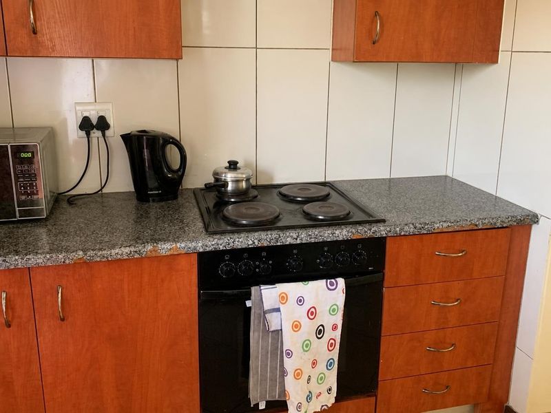 A functional kitchen area featuring wood-look cabinetry, a built-in oven with electric hob, and a tiled backsplash, showing signs of wear on the countertop.