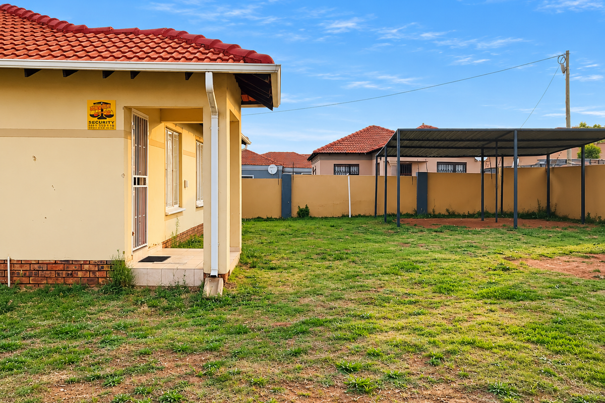 Rear view of the property featuring a tiled roof, a covered carport structure, and a spacious backyard enclosed by a perimeter wall.