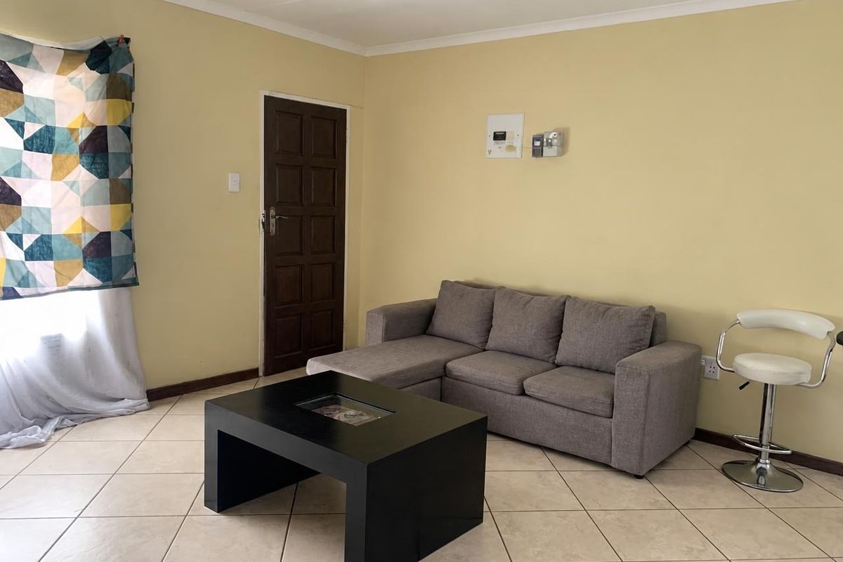 A living room featuring tiled flooring, a coved ceiling, and a timber door, providing a functional and neutral space.