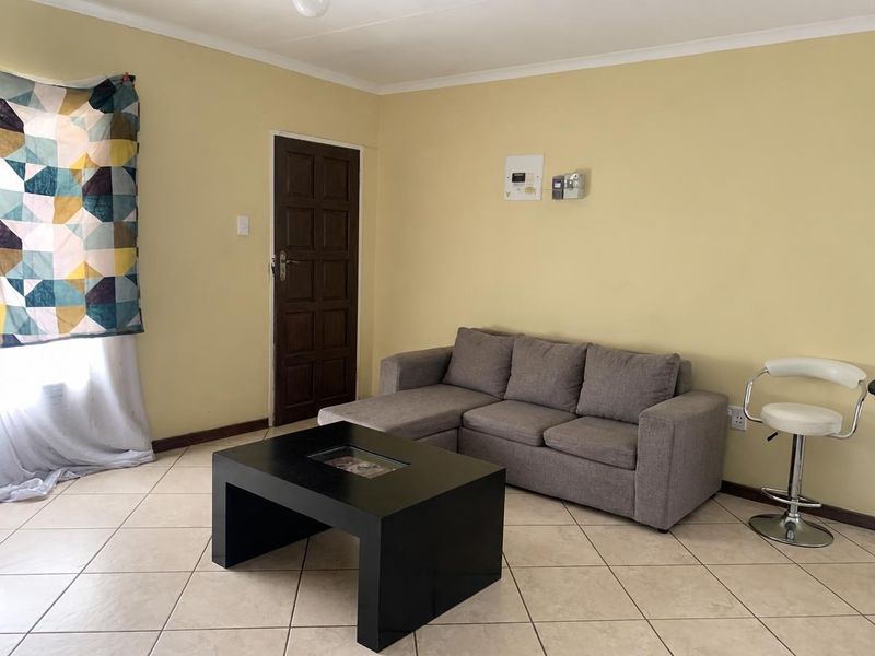 A living room featuring tiled flooring, a coved ceiling, and a timber door, providing a functional and neutral space.