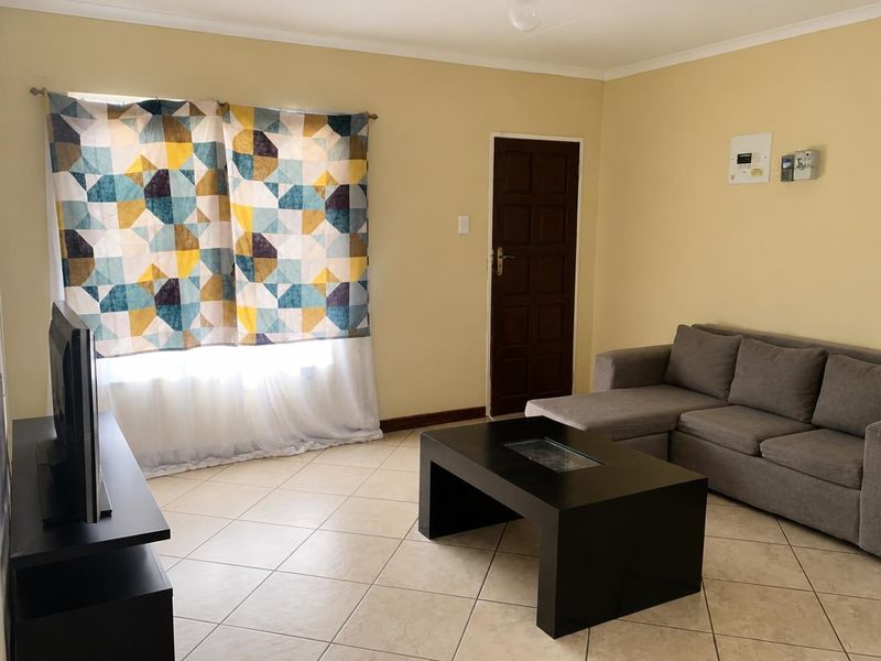 A functional living room featuring tiled flooring, a solid timber door, and a wall-mounted electrical distribution board.