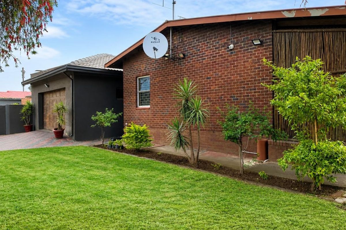 Rear view of the property featuring a brick facade, well-maintained lawn, and a paved driveway leading to a garage.