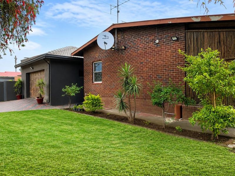 Rear view of the property featuring a brick facade, well-maintained lawn, and a paved driveway leading to a garage.