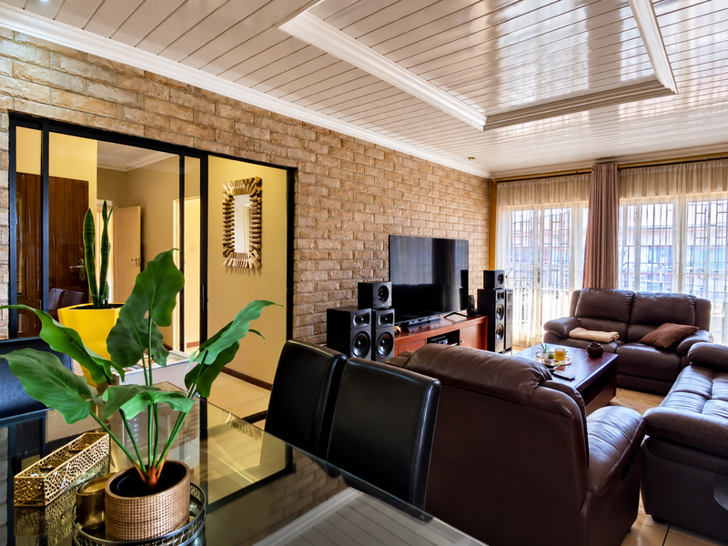 Spacious living room featuring an exposed brick feature wall, high-gloss tongue and groove ceiling, and large windows with security bars.