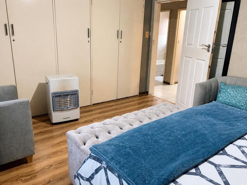 A bedroom featuring laminate flooring and built-in cupboards, with an adjacent view into a bathroom area.