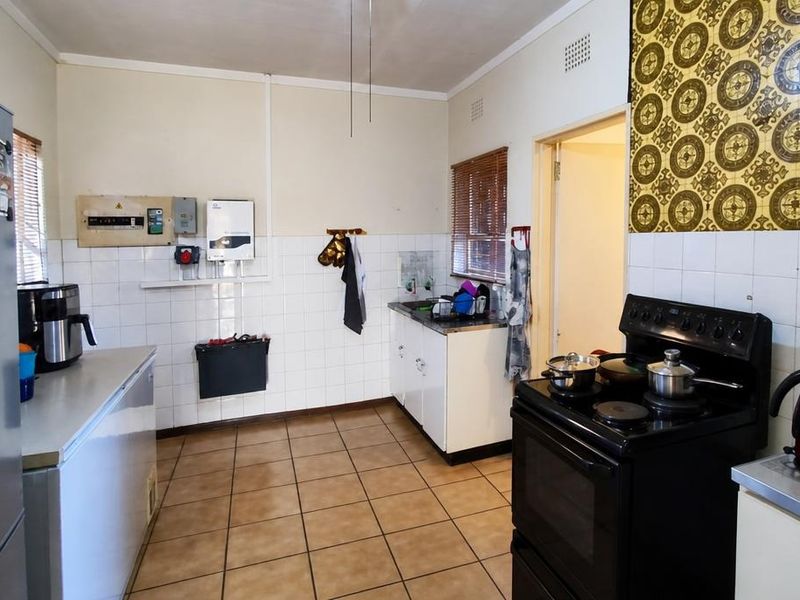 A functional kitchen featuring tiled flooring, built-in cabinetry, a sink, and an electric stove, with visible electrical infrastructure and dated wall finishes.