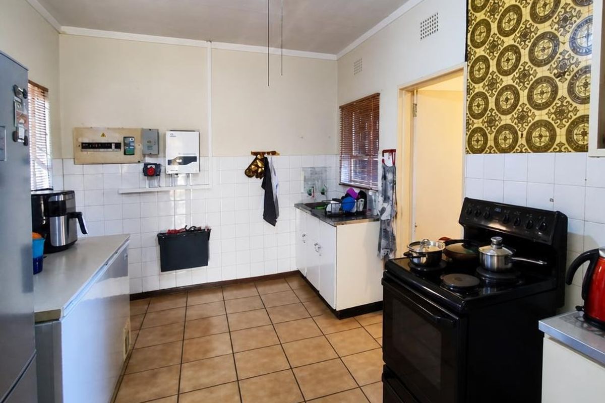 A functional kitchen featuring tiled flooring, built-in cabinetry, a sink, and an electric stove, with visible electrical infrastructure and dated wall finishes.