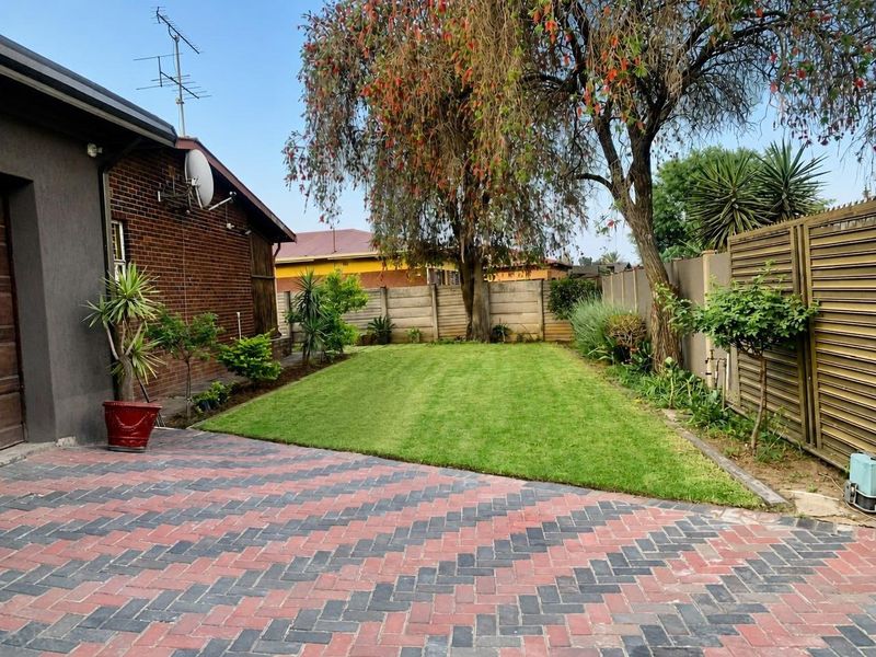 A well-maintained rear garden featuring a neat lawn, brick paving, and perimeter precast concrete walling.