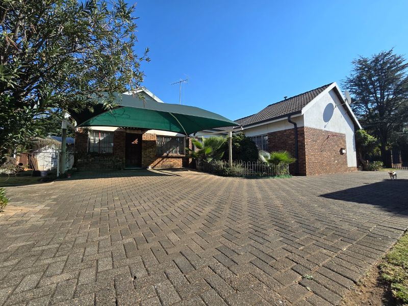 Front view of a brick house featuring a paved driveway and a large green shade sail covering the entrance area.