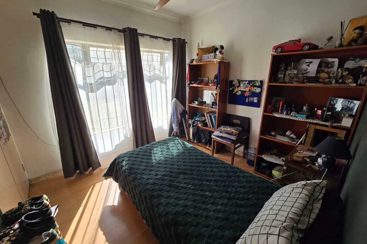 A functional bedroom featuring laminate flooring, a ceiling fan, and a window fitted with security bars for added protection.