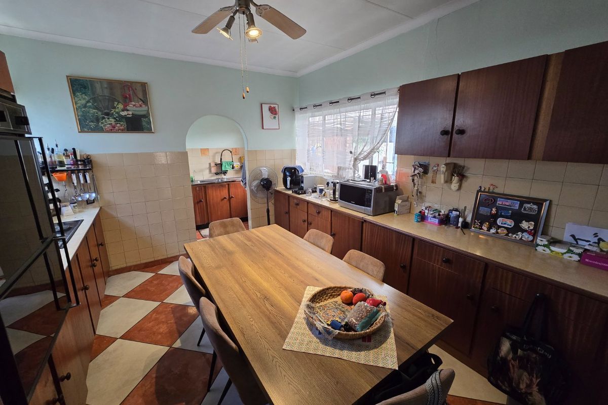 A functional kitchen featuring traditional wooden cabinetry, tiled backsplash, and a central dining area with direct access to a secondary scullery space.