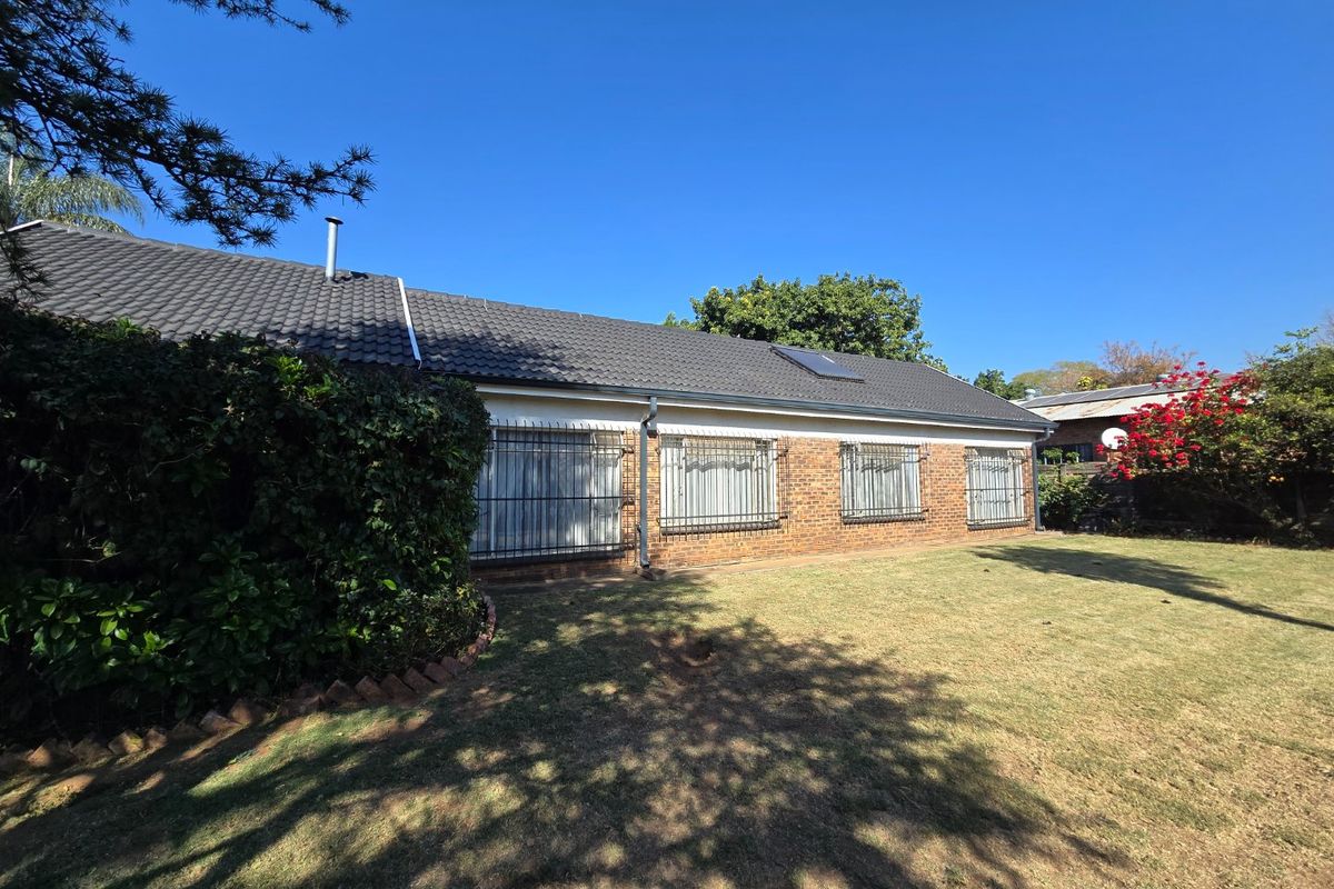 Rear view of the house featuring a brick facade, tiled roof, and security bars on the windows, set against a spacious garden.
