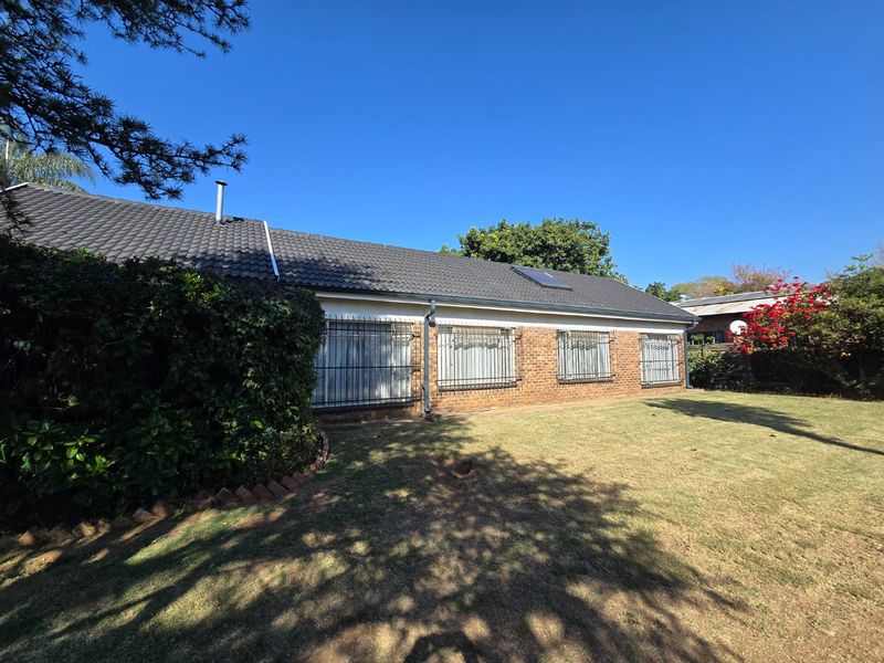 Rear view of the house featuring a brick facade, tiled roof, and security bars on the windows, set against a spacious garden.