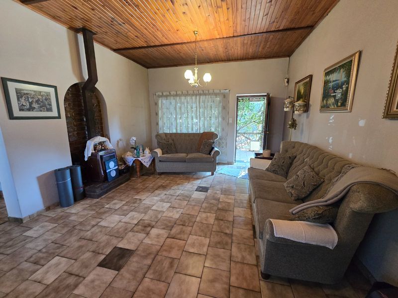A living room featuring a wood-burning fireplace with a brick surround, timber-clad ceiling, and ceramic tile flooring, with direct access to an outdoor area.