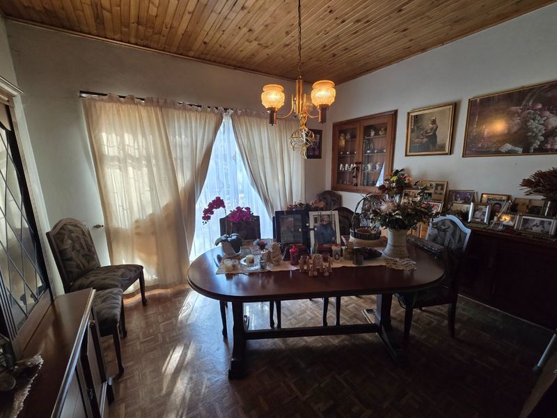 A traditional dining room featuring warm timber ceiling paneling, classic parquet flooring, and a built-in display cabinet, offering a cozy and character-filled space.