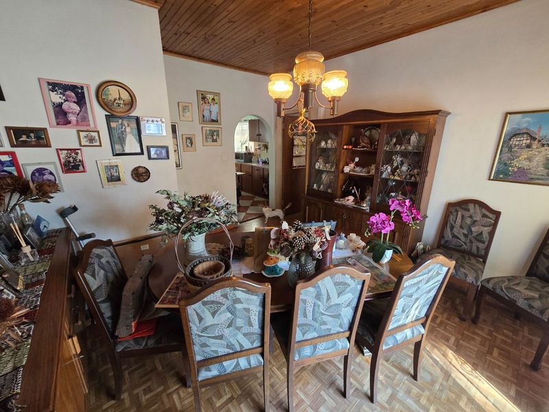 A traditional dining room featuring a timber ceiling, a central chandelier, and an arched doorway leading to the kitchen area.