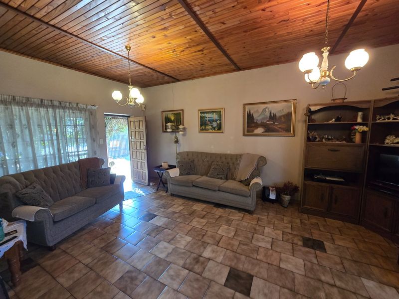 A living room featuring a timber tongue and groove ceiling, ceramic tiled flooring, and dual chandelier lighting fixtures with direct access to the exterior.