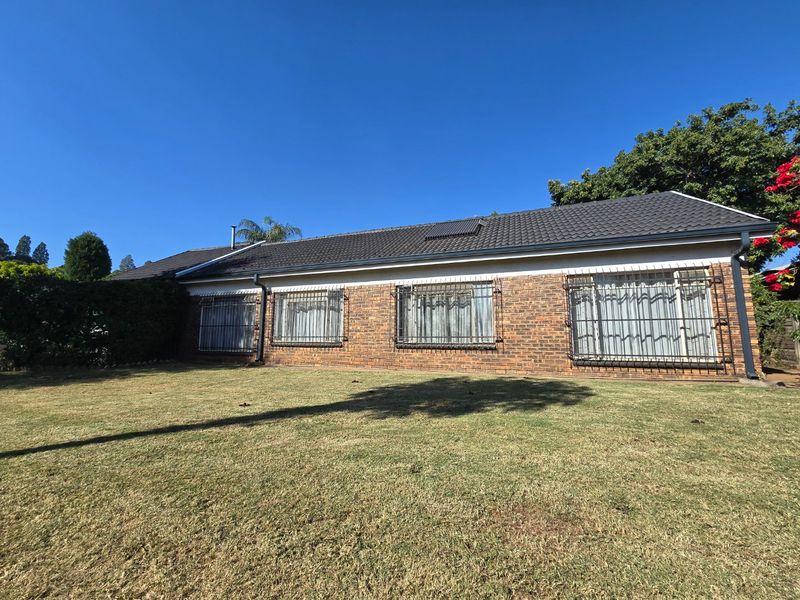 Rear view of a single-story face brick house featuring a tiled roof, security bars on windows, and a solar water heating panel.