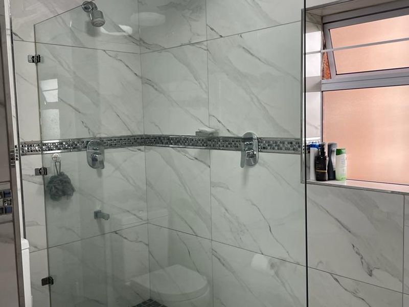 Modern bathroom featuring a spacious walk-in shower with glass screen, rainfall shower head, marble-look wall tiles, and a convenient built-in shower niche.