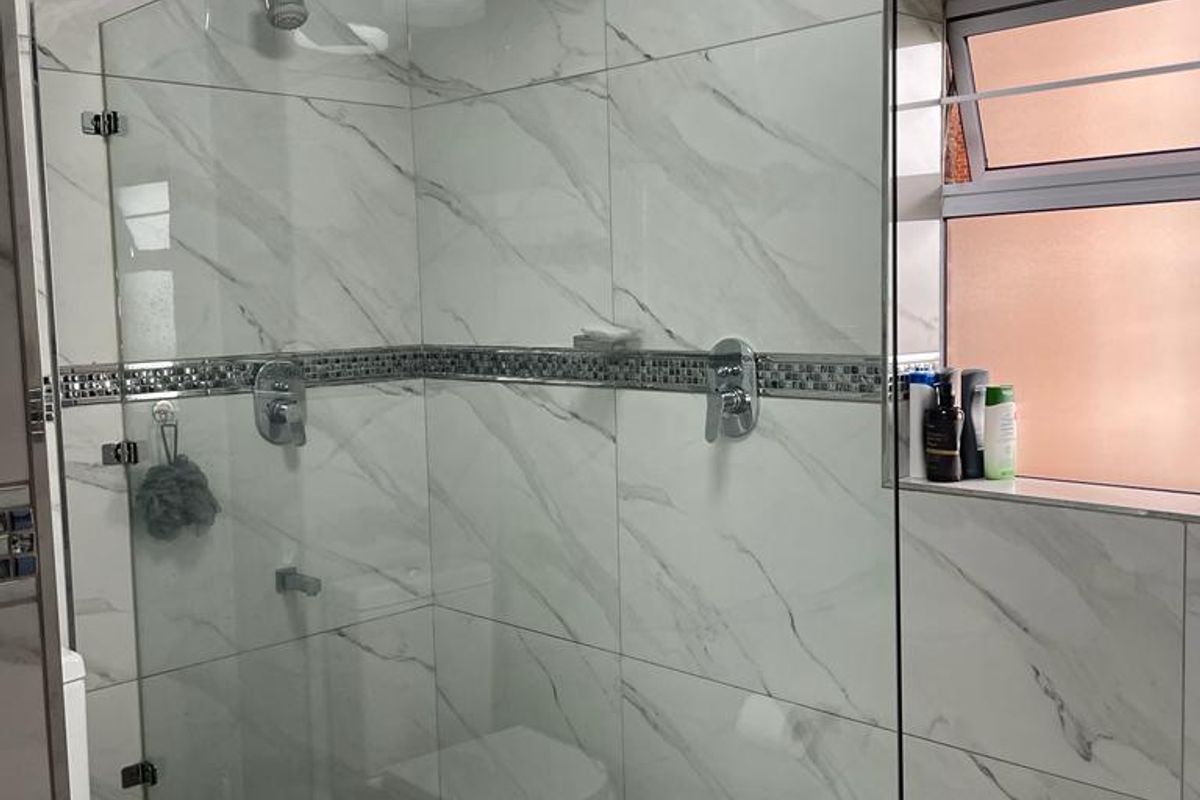 Modern bathroom featuring a spacious walk-in shower with glass screen, rainfall shower head, marble-look wall tiles, and a convenient built-in shower niche.