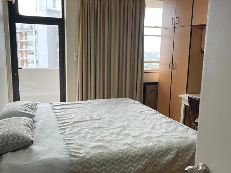 A functional bedroom featuring built-in cupboards, a ceiling fan, and access to a balcony, providing natural light and practical storage solutions.
