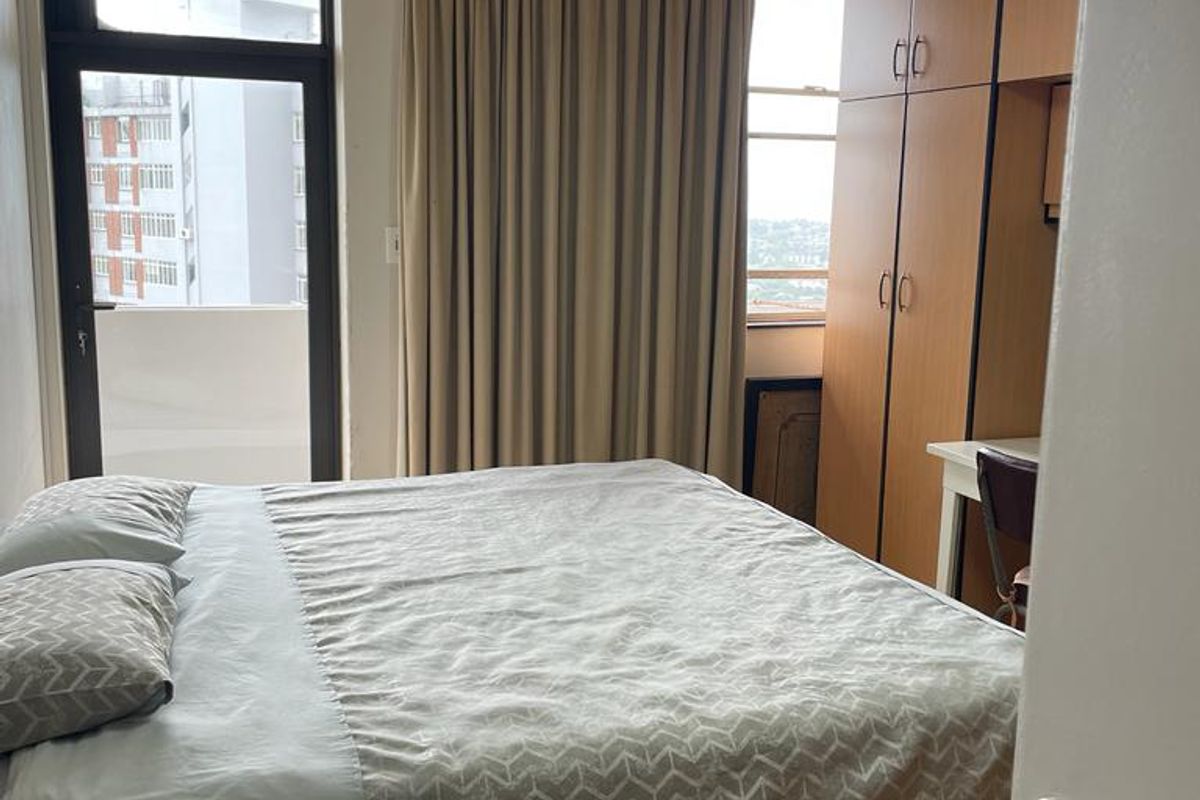 A functional bedroom featuring built-in cupboards, a ceiling fan, and access to a balcony, providing natural light and practical storage solutions.