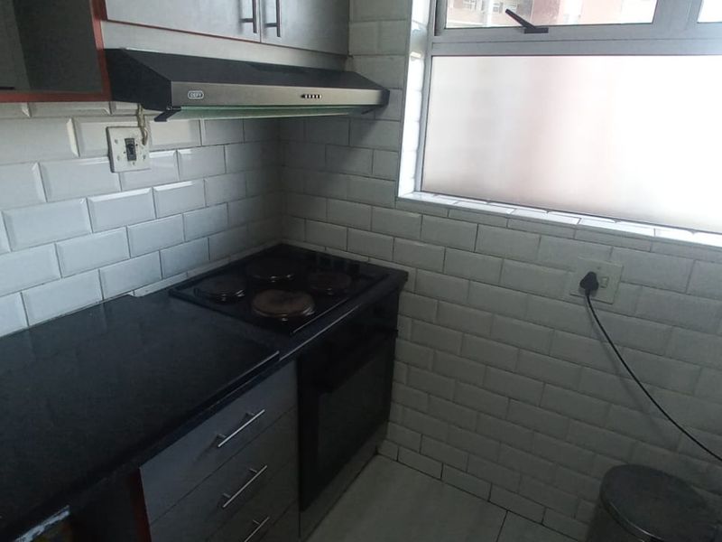 A compact kitchen featuring subway tile backsplash, black granite countertops, built-in oven and stove, and grey cabinetry with an extractor fan.