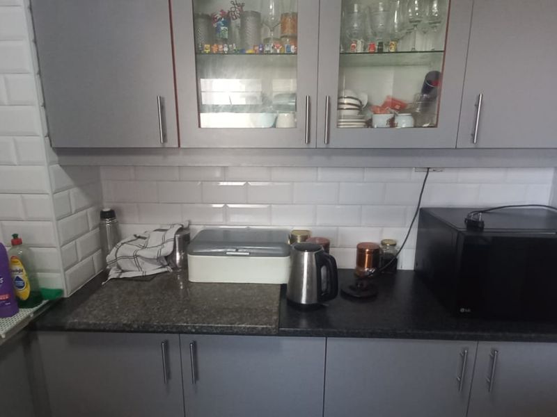 A functional kitchen area featuring grey cabinetry, a white subway tile backsplash, and dark laminate countertops with integrated sink and storage space.