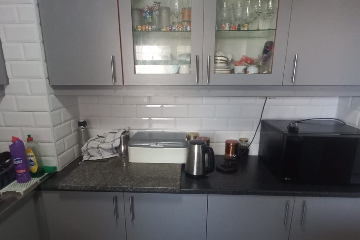 A functional kitchen area featuring grey cabinetry, a white subway tile backsplash, and dark laminate countertops with integrated sink and storage space.