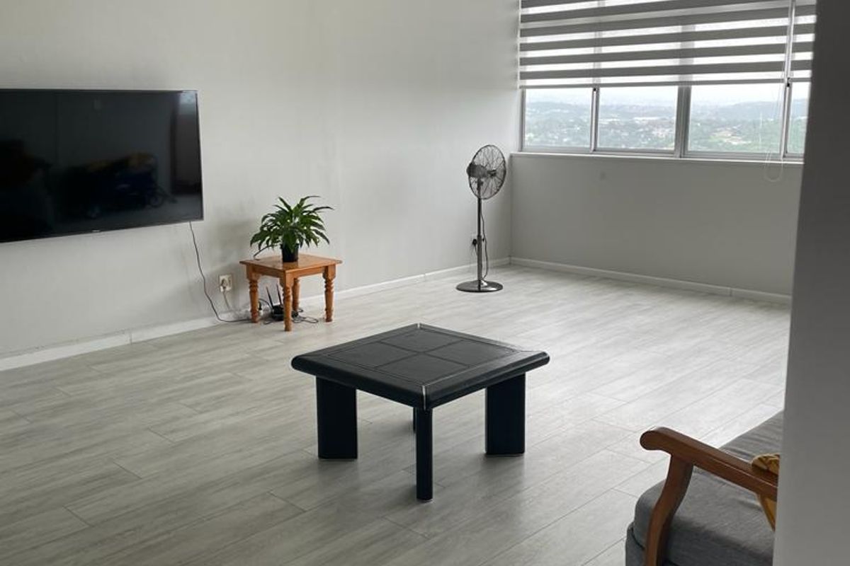 Spacious living room featuring light-toned laminate flooring, large windows with modern roller blinds, and a decorative ceiling light fixture.