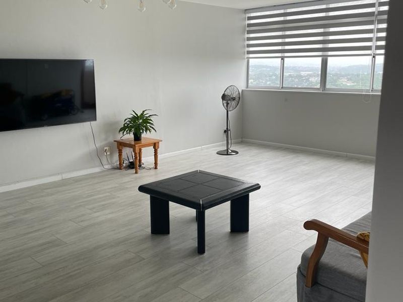 Spacious living room featuring light-toned laminate flooring, large windows with modern roller blinds, and a decorative ceiling light fixture.