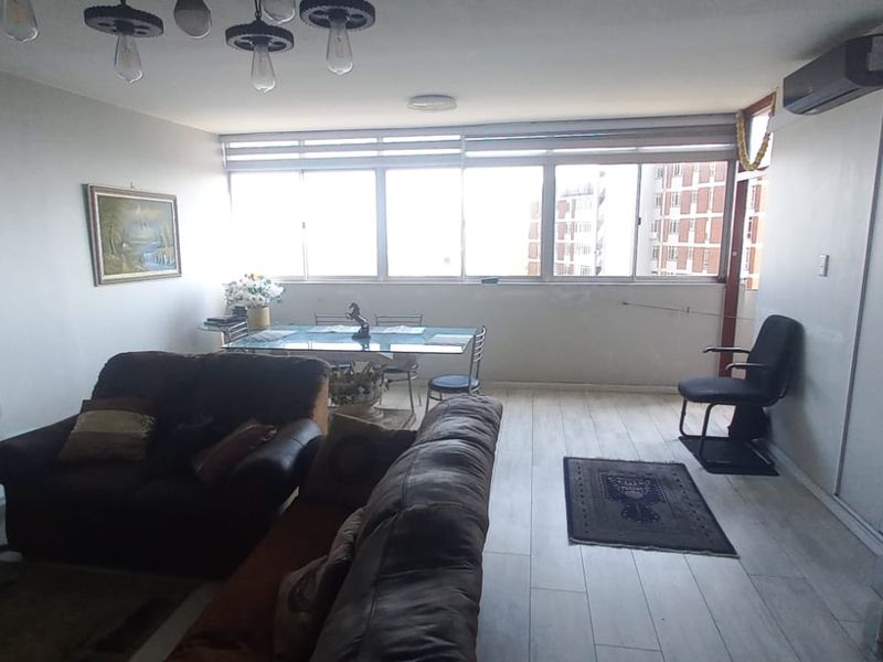 Spacious living and dining area featuring laminate flooring, large windows providing natural light, and a wall-mounted air conditioning unit.
