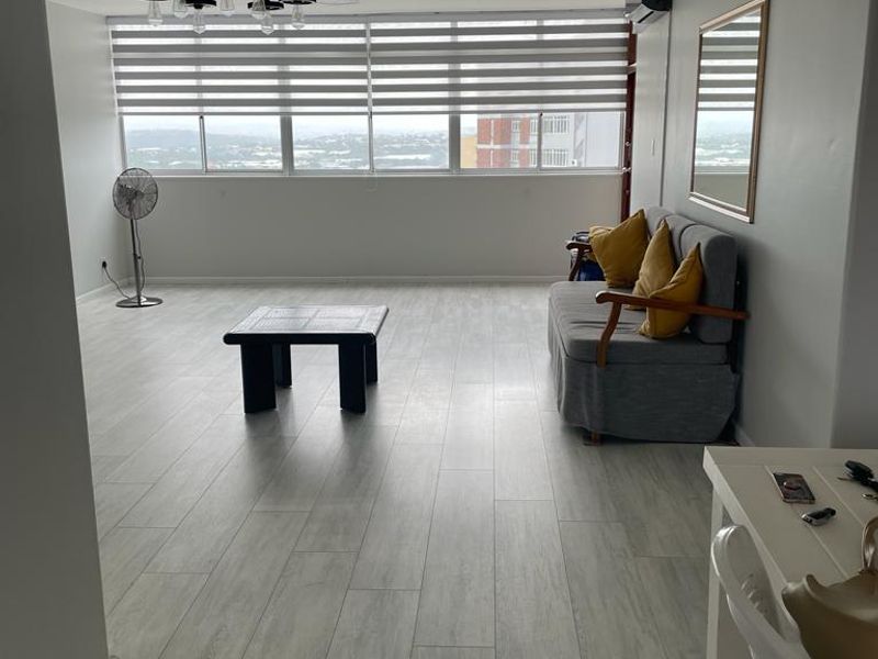 Spacious living area featuring light wood-look tile flooring, large windows with roller blinds, and a wall-mounted air conditioning unit.