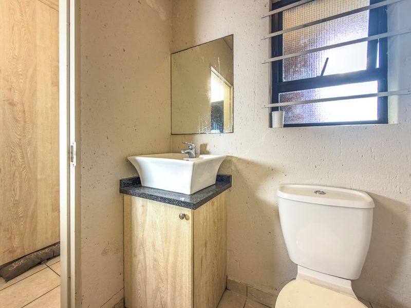 A compact bathroom featuring a vessel sink on a vanity cabinet, a toilet, and a window with security bars, requiring cosmetic updates.