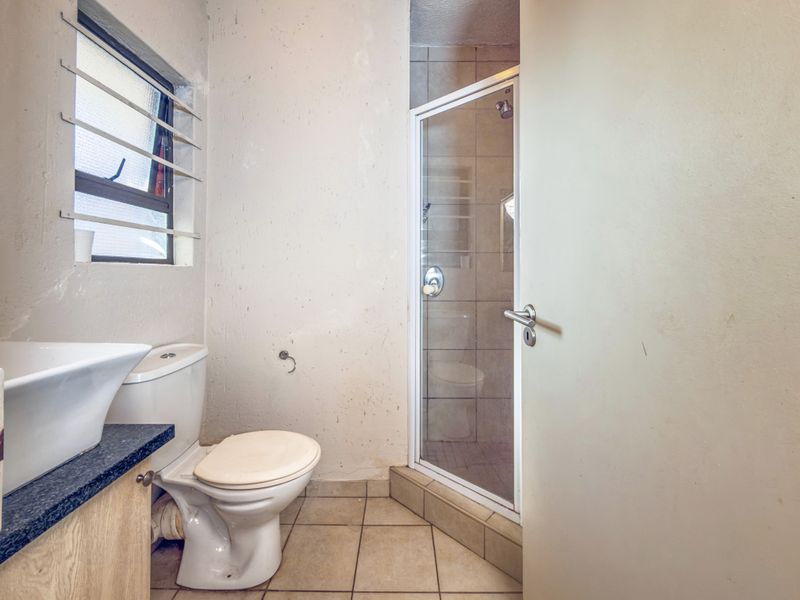 A functional bathroom featuring a shower enclosure, toilet, and vanity basin with tiled flooring and louver windows.