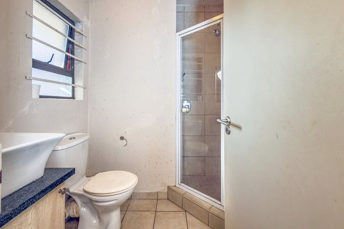 A functional bathroom featuring a shower enclosure, toilet, and vanity basin with tiled flooring and louver windows.