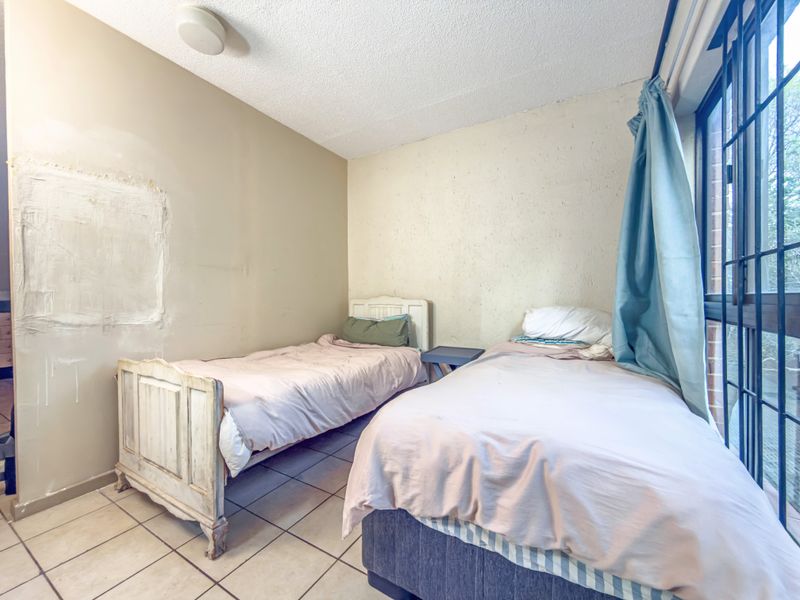 A bedroom featuring tiled flooring and a large window with security bars, currently requiring wall repairs and cosmetic updates.
