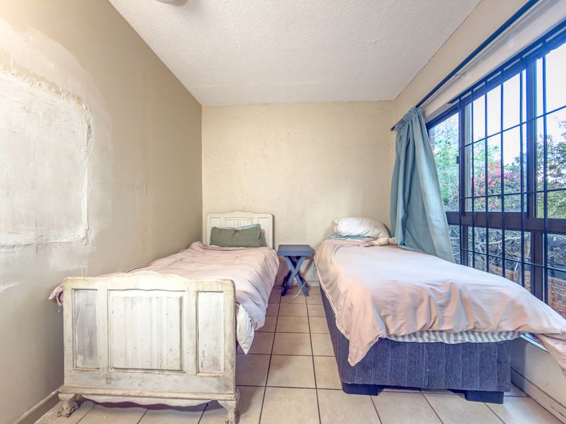 A bedroom featuring tiled flooring and a large sliding glass door with security bars, currently requiring wall repairs and cosmetic updates.