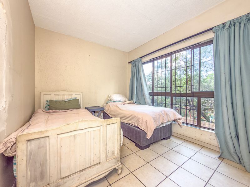 A bedroom featuring tiled flooring and a large window with security bars, offering natural light and views of the surrounding greenery.