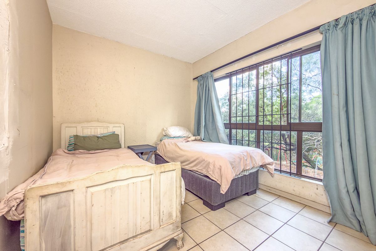 A bedroom featuring tiled flooring and a large window with security bars, offering natural light and views of the surrounding greenery.