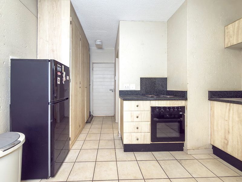 A functional kitchen featuring built-in cabinetry, laminate countertops, and an integrated oven with electric hob, finished with tiled flooring.
