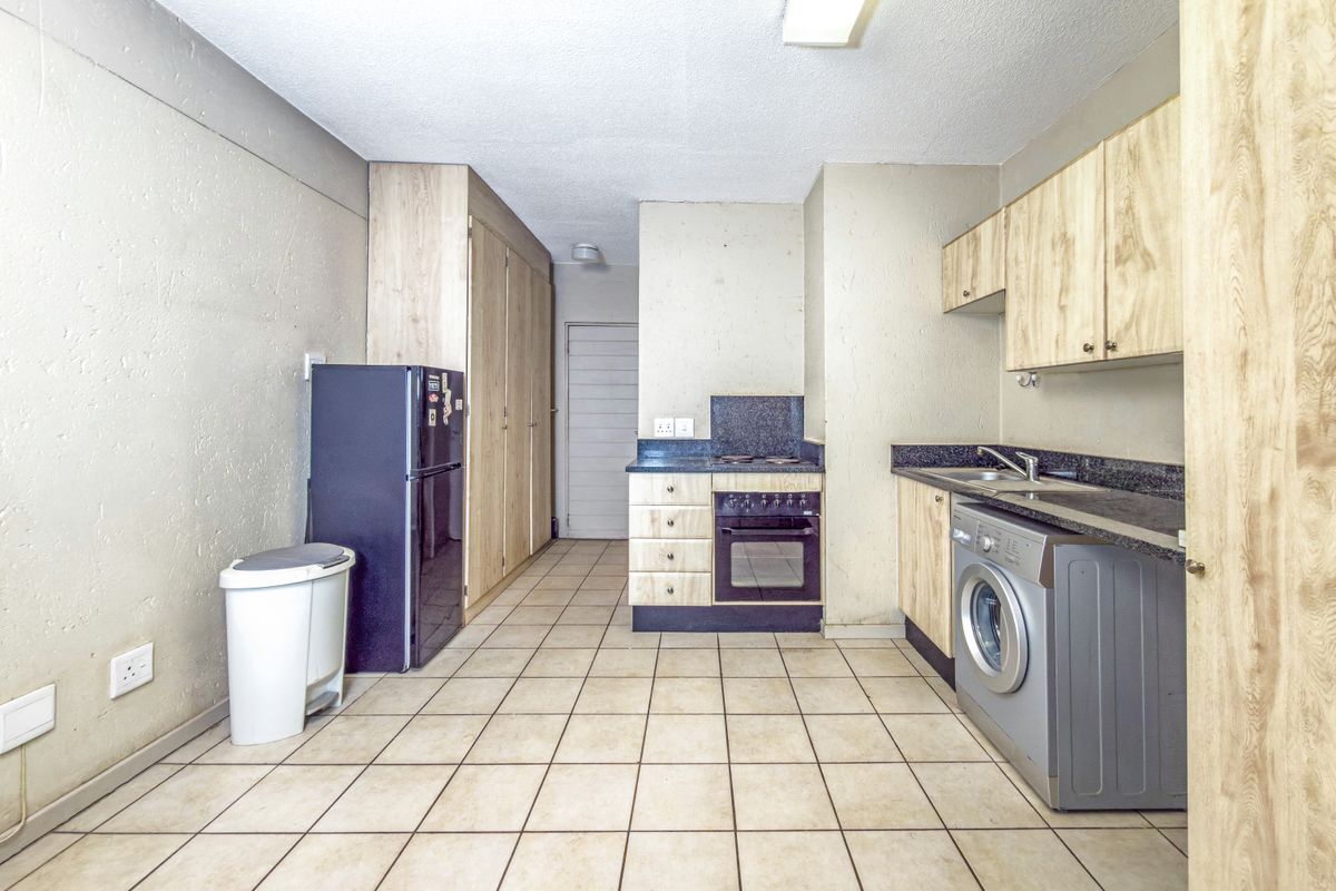 Functional kitchen featuring light wood-finish cabinetry, dark laminate countertops, built-in oven and hob, and tiled flooring with ample storage space.
