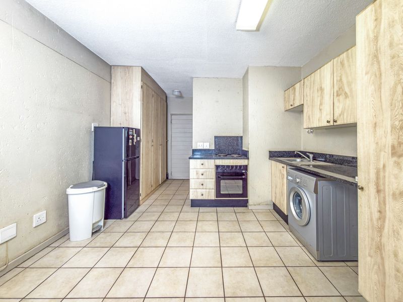 Functional kitchen featuring light wood-finish cabinetry, dark laminate countertops, built-in oven and hob, and tiled flooring with ample storage space.