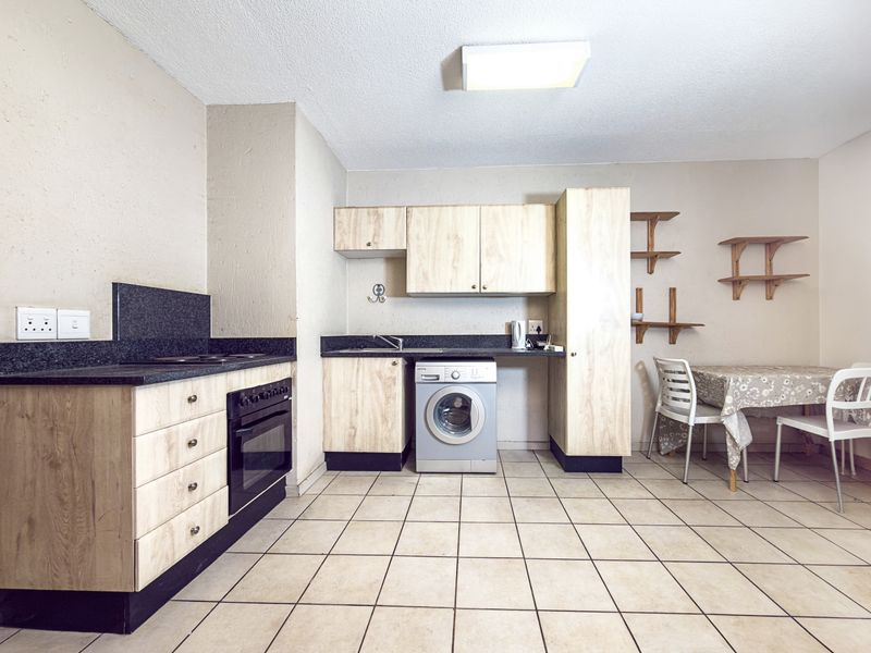 Functional kitchen featuring light wood-finish cabinetry, dark laminate countertops, built-in oven, hob, and dedicated plumbing for a washing machine.
