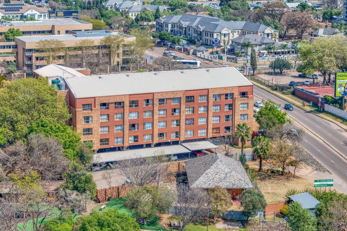 Aerial view of a multi-story brick apartment building featuring a metal roof and ground-level covered parking, situated in a suburban neighborhood.